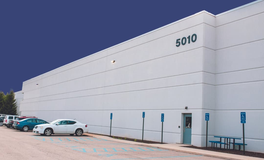 White precast concrete industrial building marked 5010, with cars parked along its side under a clear sky