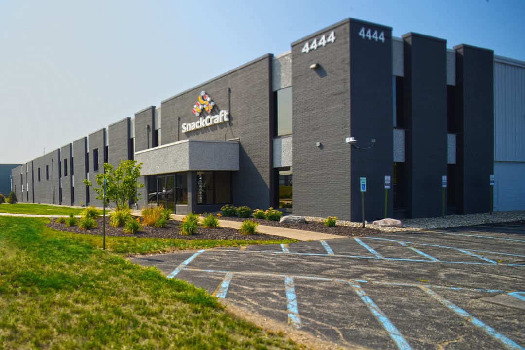 The SnackCraft building at 4444 52nd Street in Kentwood, Michigan: a dark grey two-story office front marked 4444, with the plant running back from it and a parking lot in front