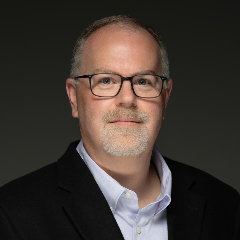 Studio portrait of Ryan Van Dam, Controller of Carbon River Capital, in a dark jacket and glasses